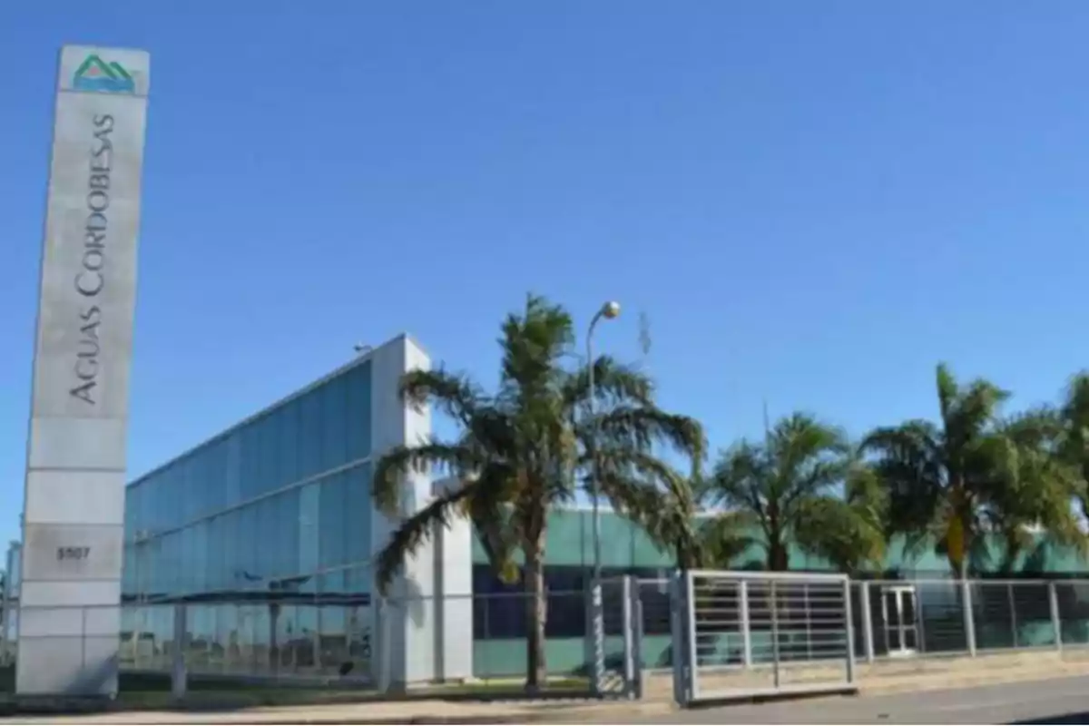 Modern glass building with palm trees in front and a sign that reads Aguas Cordobesas under a clear sky Modern glass building with palm trees in front and a sign that reads Aguas Cordobesas under a clear sky