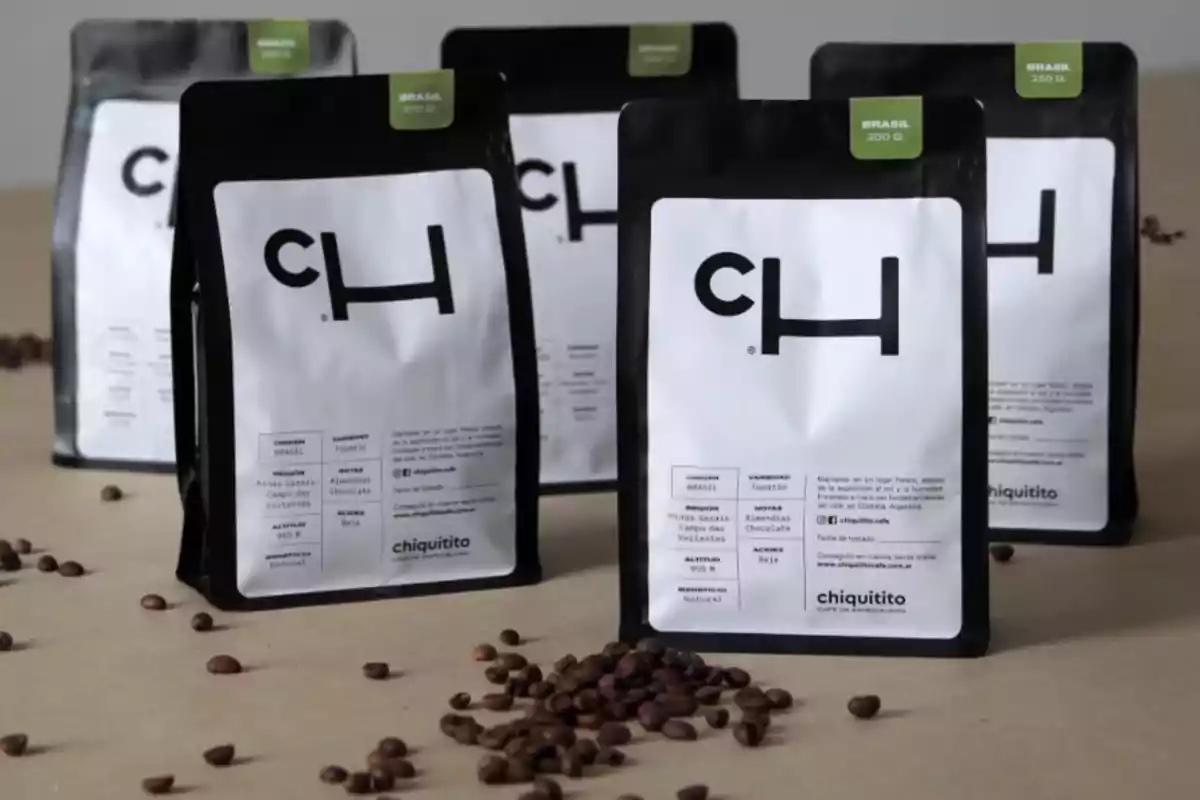 Five bags of Chiquitito brand coffee on a beige surface with coffee beans scattered in front. Five bags of Chiquitito brand coffee on a beige surface with coffee beans scattered in front.