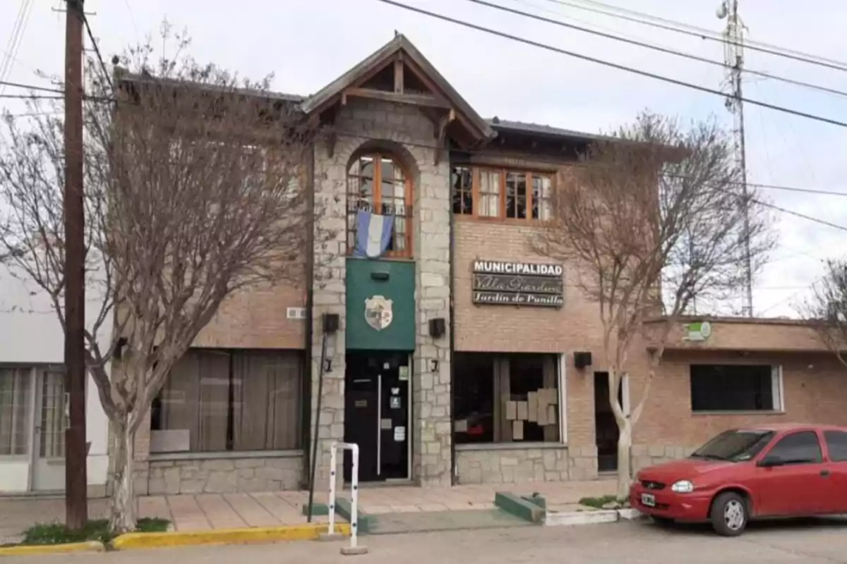 Facade of a municipal building made of stone and brick with a red car parked in front and leafless trees
