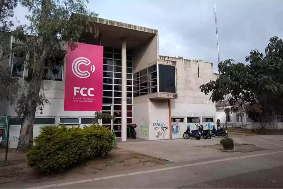 Faculty of Communication Sciences building with a pink sign at the entrance, some trees, and motorcycles parked in front Faculty of Communication Sciences building with a pink sign at the entrance, some trees, and motorcycles parked in front