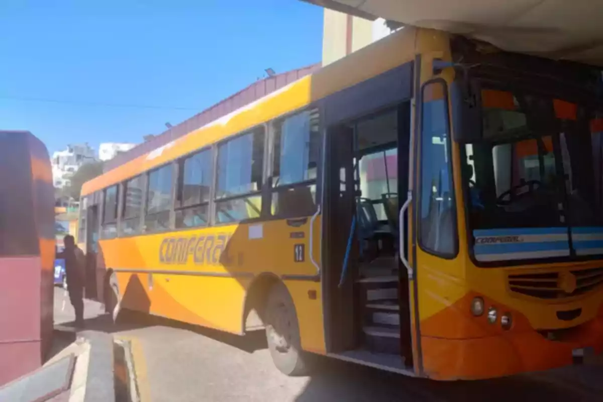 Yellow bus stuck at the entrance of a terminal with the door open and a person standing nearby Yellow bus stuck at the entrance of a terminal with the door open and a person standing nearby