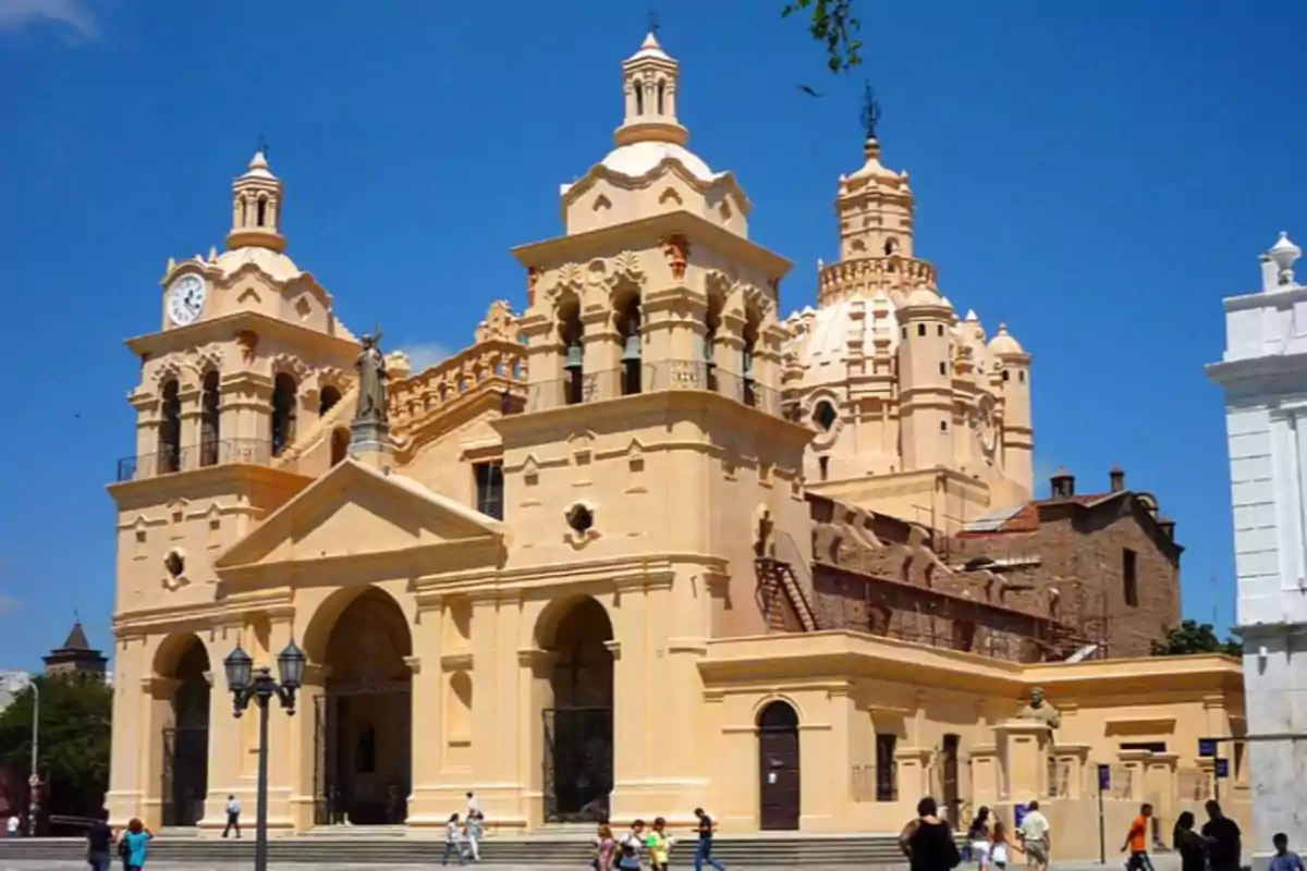 Colonial-style cathedral with towers and a yellow dome under a clear sky, with people walking in the square in front of the building