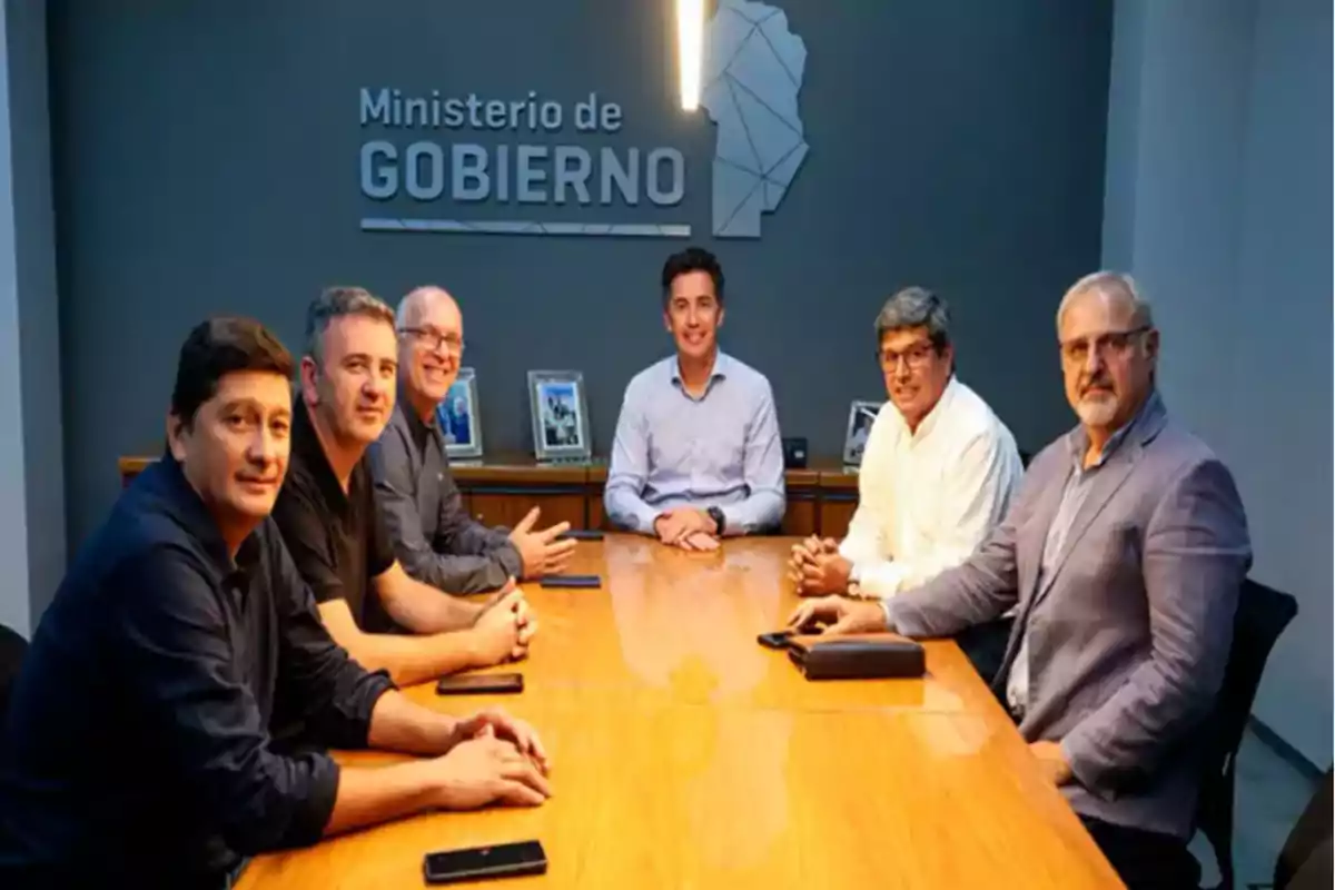 Six men sitting around a conference table in an office with a Ministry of Government sign on the back wall Six men sitting around a conference table in an office with a Ministry of Government sign on the back wall