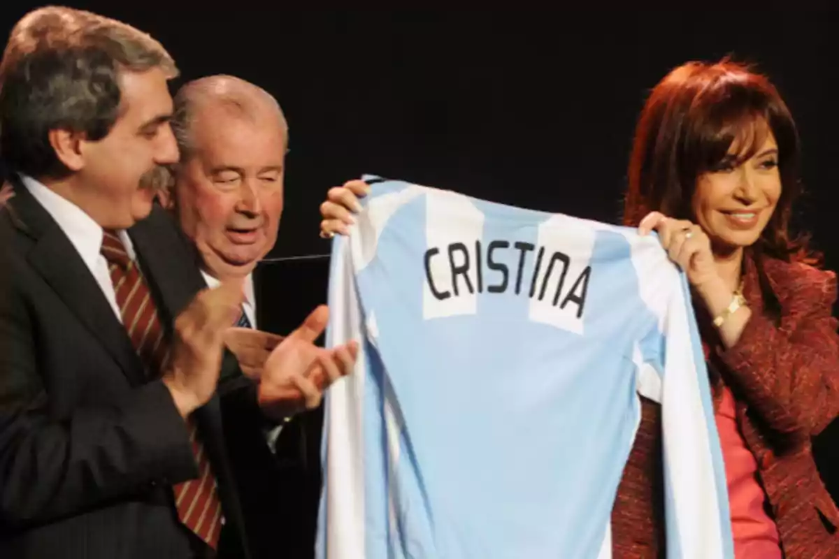 Three people smile while one of them holds an Argentina national team jersey with the name Cristina on the back.