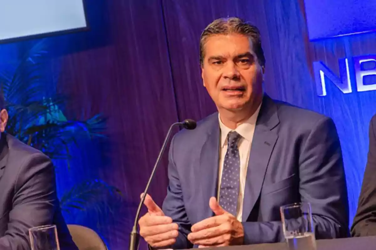 Man in a blue suit speaking at a conference with a microphone and a blue background Man in a blue suit speaking at a conference with a microphone and a blue background