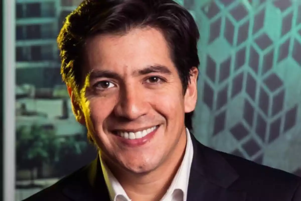 Hombre de cabello oscuro con traje y camisa blanca sonriendo frente a un fondo de oficina desenfocado Hombre de cabello oscuro con traje y camisa blanca sonriendo frente a un fondo de oficina desenfocado
