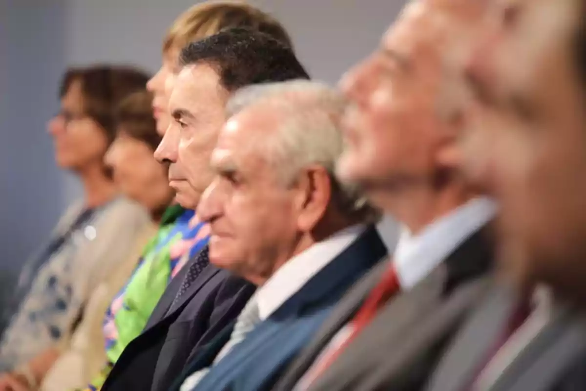 Group of people seated in a row alertly watching in the same direction at a formal event Group of people seated in a row alertly watching in the same direction at a formal event