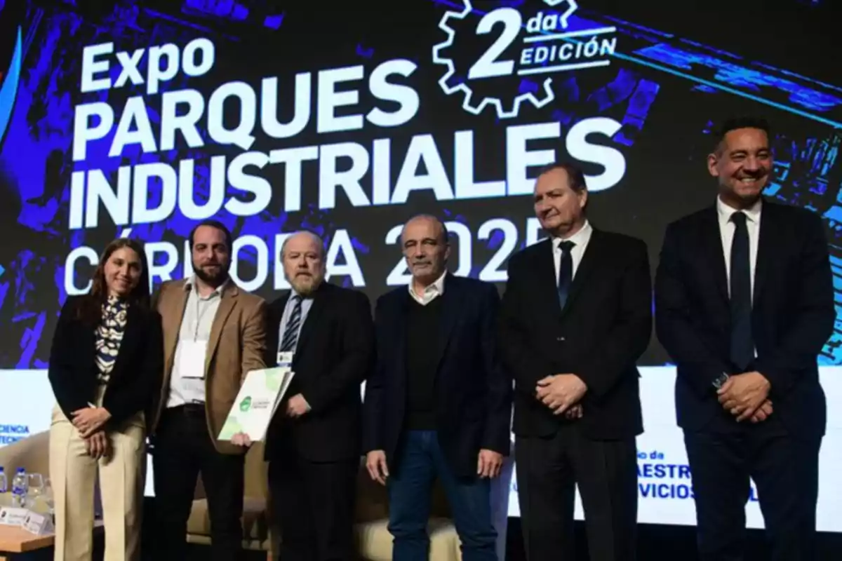 Six people pose for a photo on the stage of a business event with a background sign that reads Expo Parques Industriales Córdoba 2023 2nd edition.