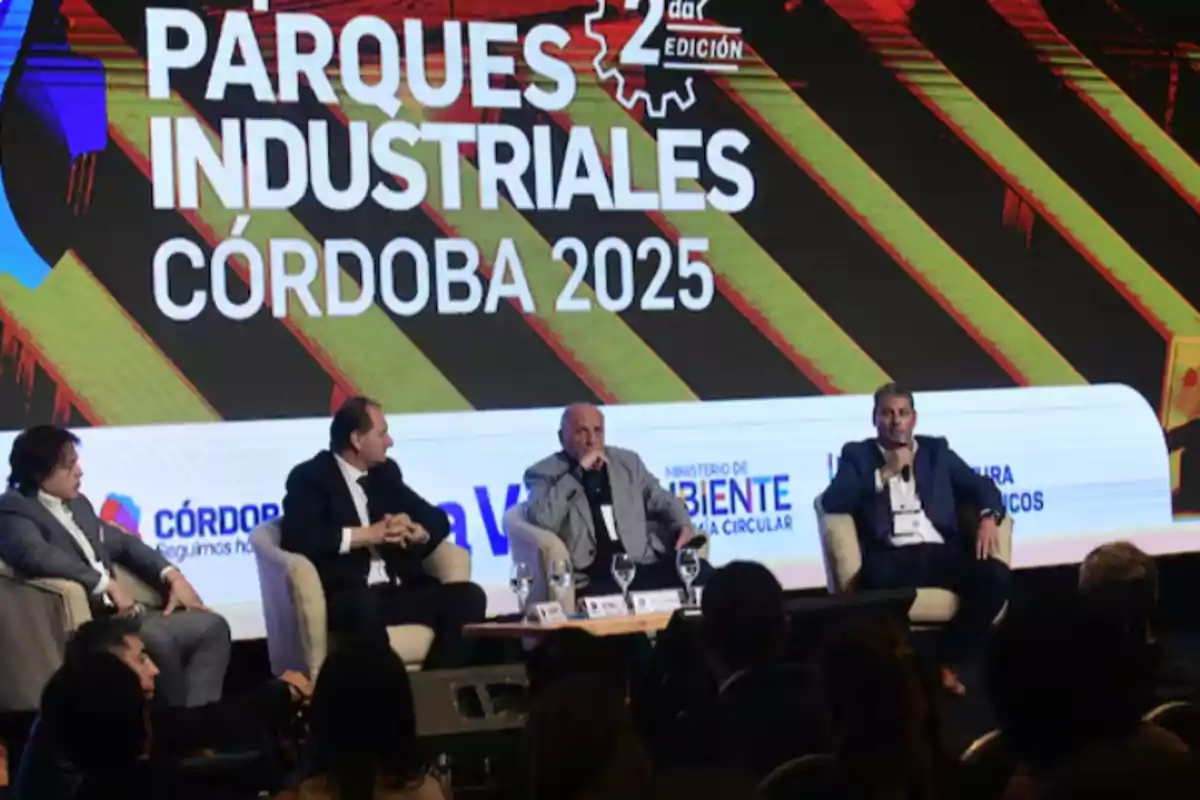 Four men seated in armchairs participate in a panel discussion at an event titled Córdoba Industrial Parks 2025, with a large screen in the background and an audience watching. Four men seated in armchairs participate in a panel discussion at an event titled Córdoba Industrial Parks 2025, with a large screen in the background and an audience watching.