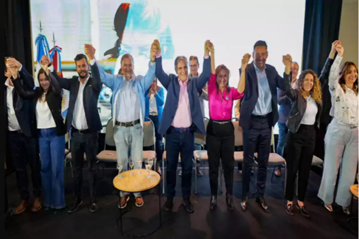 Group of people standing on a stage raising their joined hands in a gesture of celebration or support