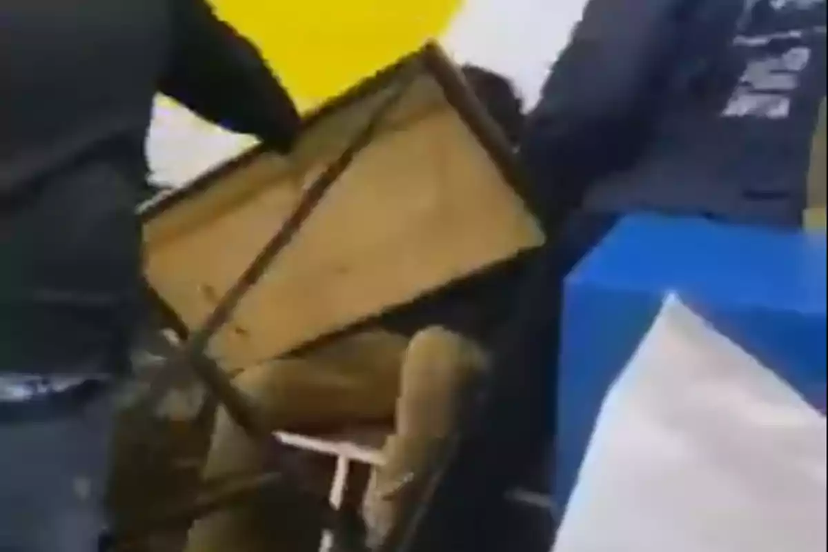 Persona cubriéndose con una mesa durante un altercado en un entorno con manteles de colores vivos Persona cubriéndose con una mesa durante un altercado en un entorno con manteles de colores vivos