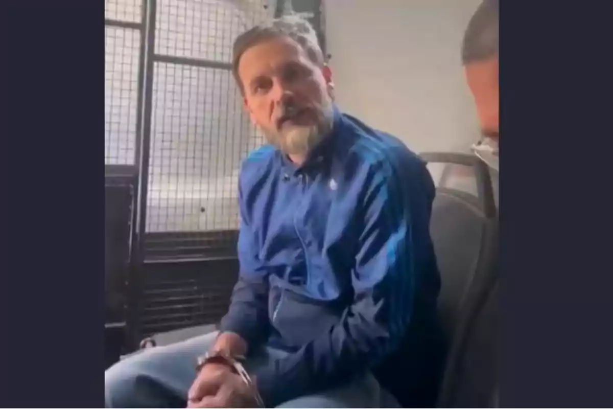 Hombre con barba y chaqueta azul sentado esposado dentro de un vehículo policial