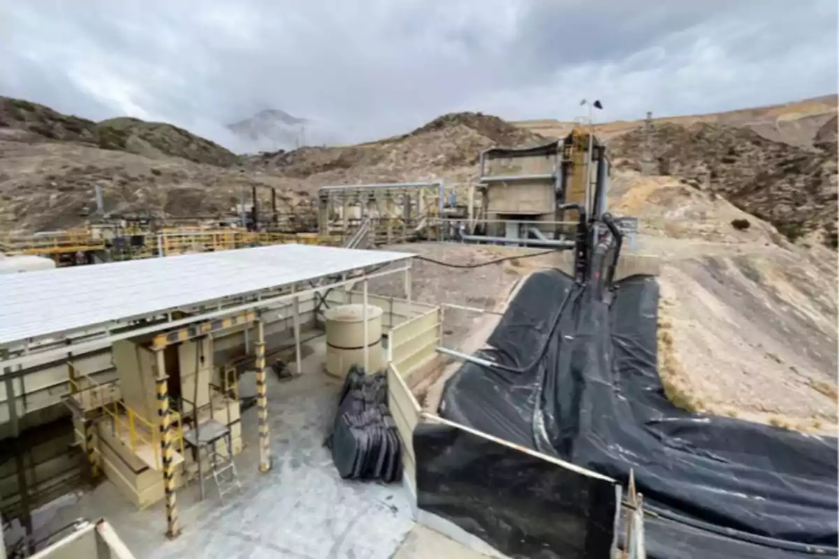 Instalaciones industriales en una zona montañosa con estructuras metálicas y tuberías junto a una pendiente cubierta con lona negra
