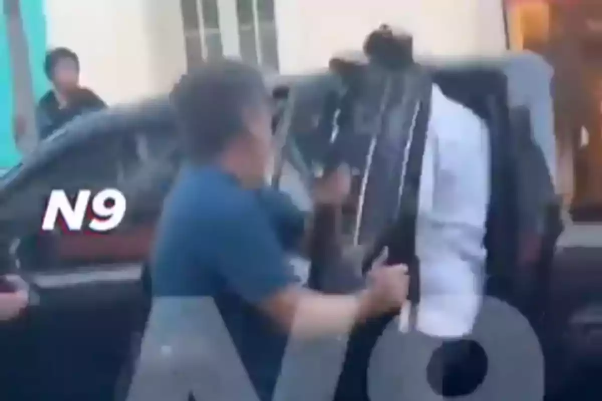 A man is holding a guitar while arguing with another person next to a black car on the street.