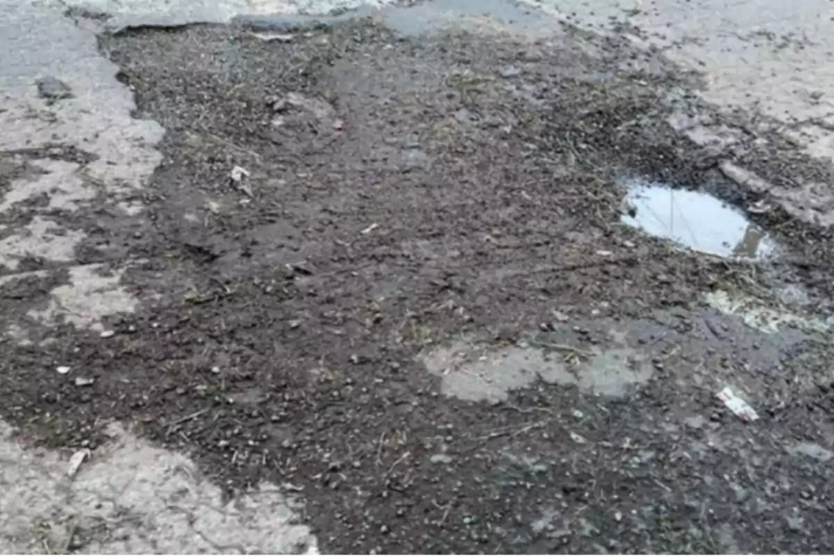 Large pothole on a street with a puddle of water and accumulated dirt Large pothole on a street with a puddle of water and accumulated dirt
