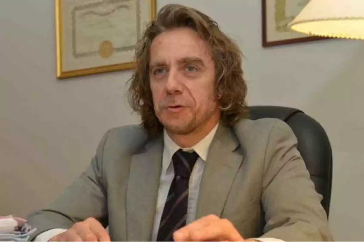 Hombre de cabello largo y rubio con traje gris sentado en una oficina Hombre de cabello largo y rubio con traje gris sentado en una oficina