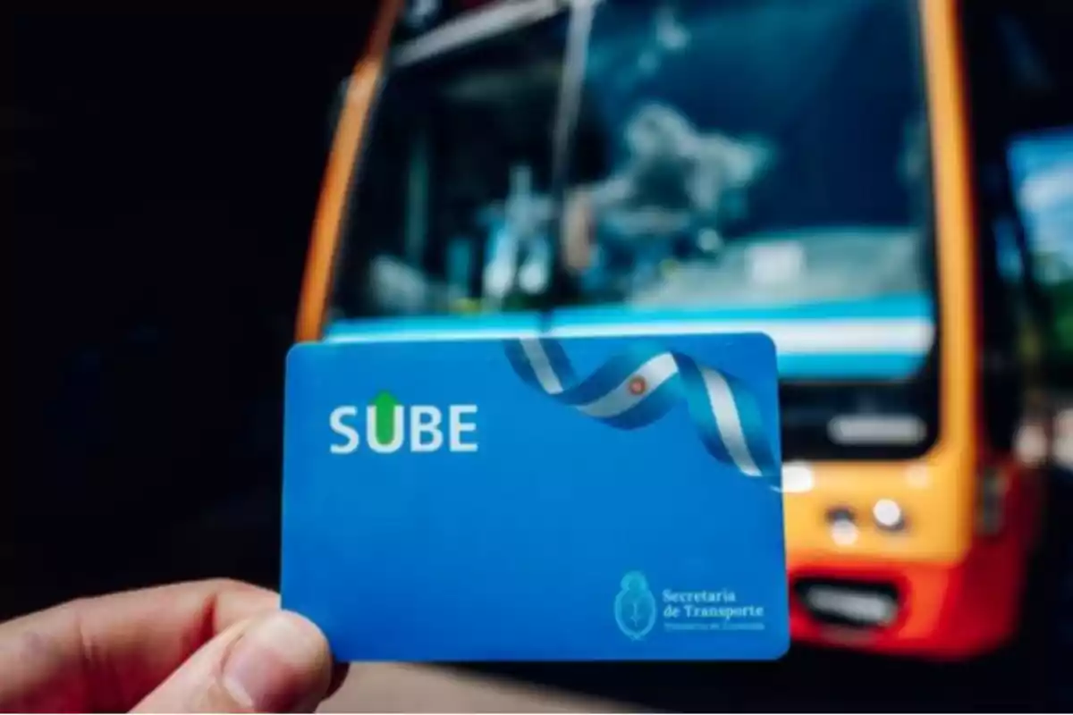 Persona sosteniendo una tarjeta SUBE frente a un colectivo en la calle