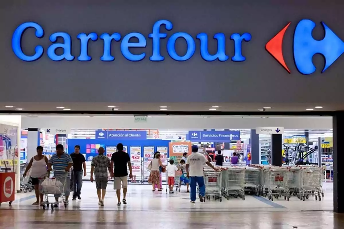Entrada de un supermercado Carrefour con varias personas entrando y saliendo y carritos de compras en la entrada Entrada de un supermercado Carrefour con varias personas entrando y saliendo y carritos de compras en la entrada