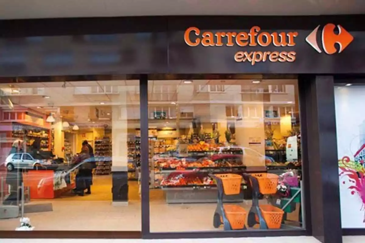 Fachada de un supermercado Carrefour Express con ventanales grandes y carritos naranjas en la entrada Fachada de un supermercado Carrefour Express con ventanales grandes y carritos naranjas en la entrada