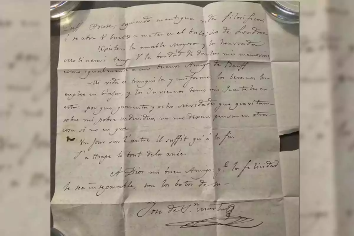 Old handwritten letter on folded paper, written in black ink with cursive handwriting, on a table and partially held down by two circular objects at the upper corners. Old handwritten letter on folded paper, written in black ink with cursive handwriting, on a table and partially held down by two circular objects at the upper corners.