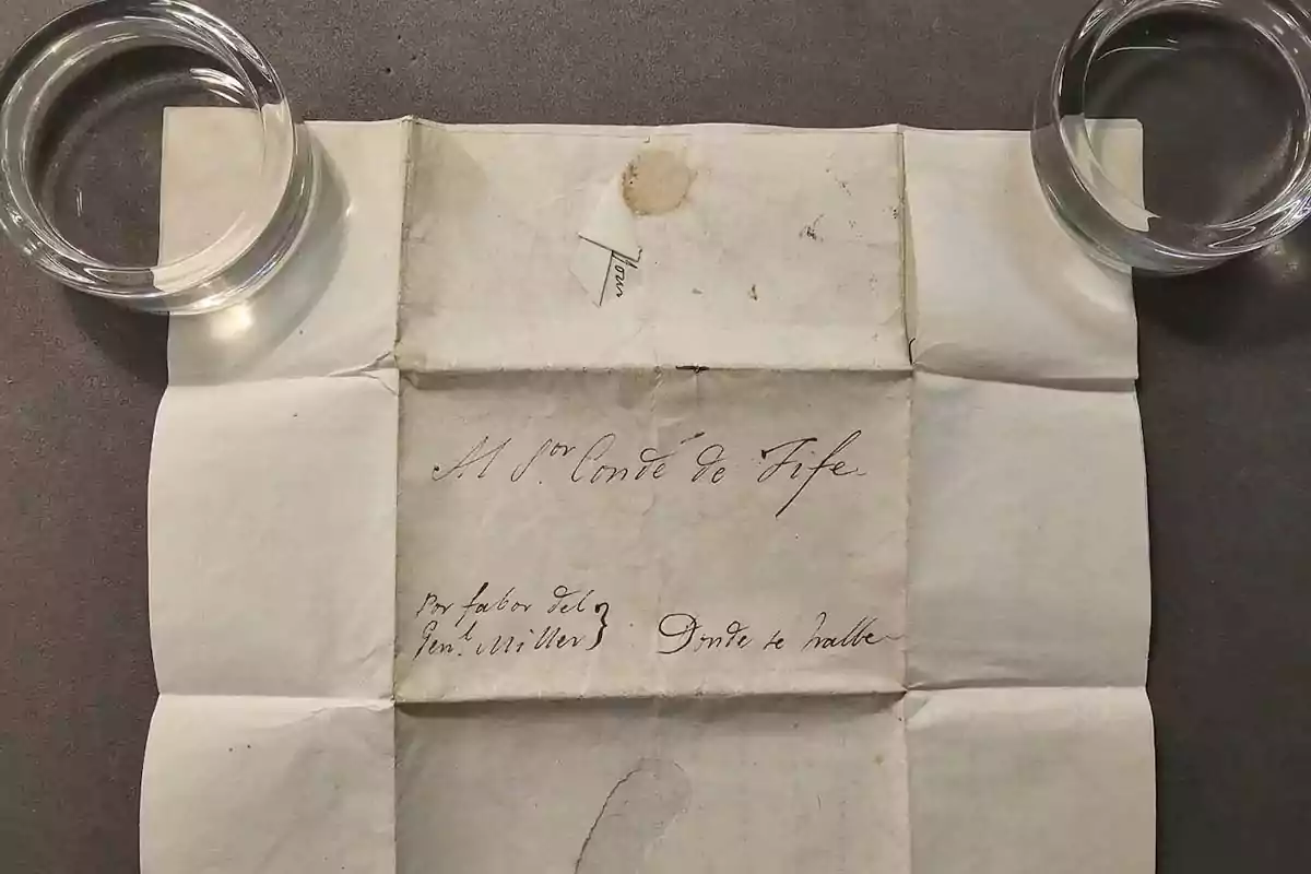Old handwritten document on folded paper held by two circular glass objects at the upper corners Old handwritten document on folded paper held by two circular glass objects at the upper corners