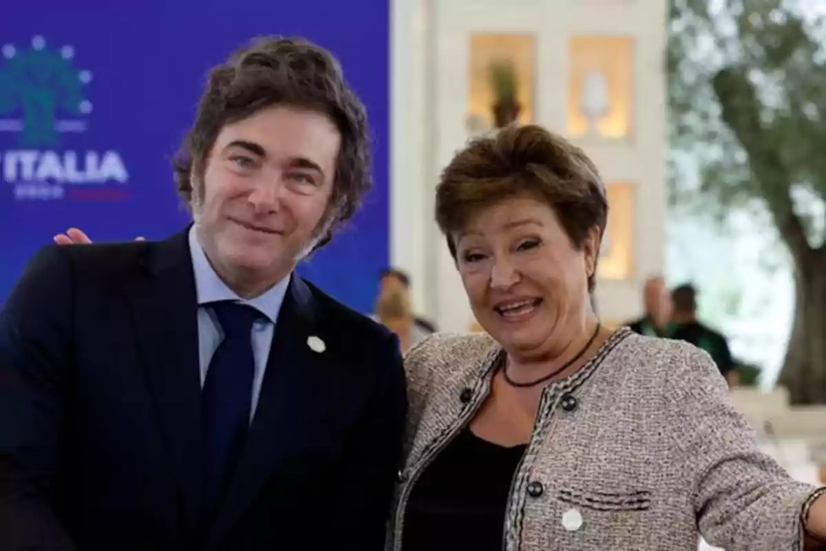 Dos personas sonríen y posan juntas en un evento formal con fondo azul y decoración elegante. Dos personas sonríen y posan juntas en un evento formal con fondo azul y decoración elegante.