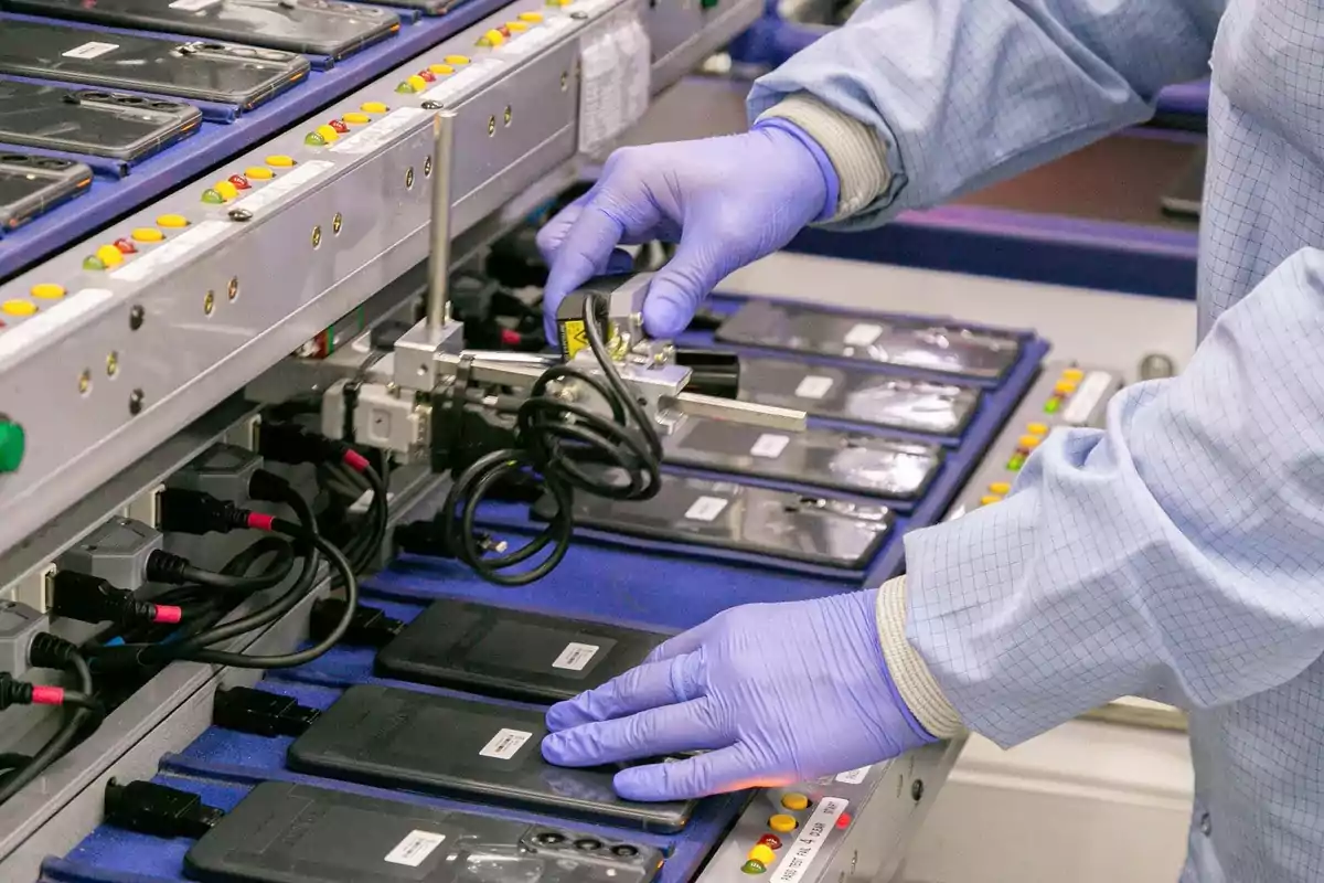 Person wearing gloves and a lab coat handling mobile phones on an industrial assembly line Person wearing gloves and a lab coat handling mobile phones on an industrial assembly line