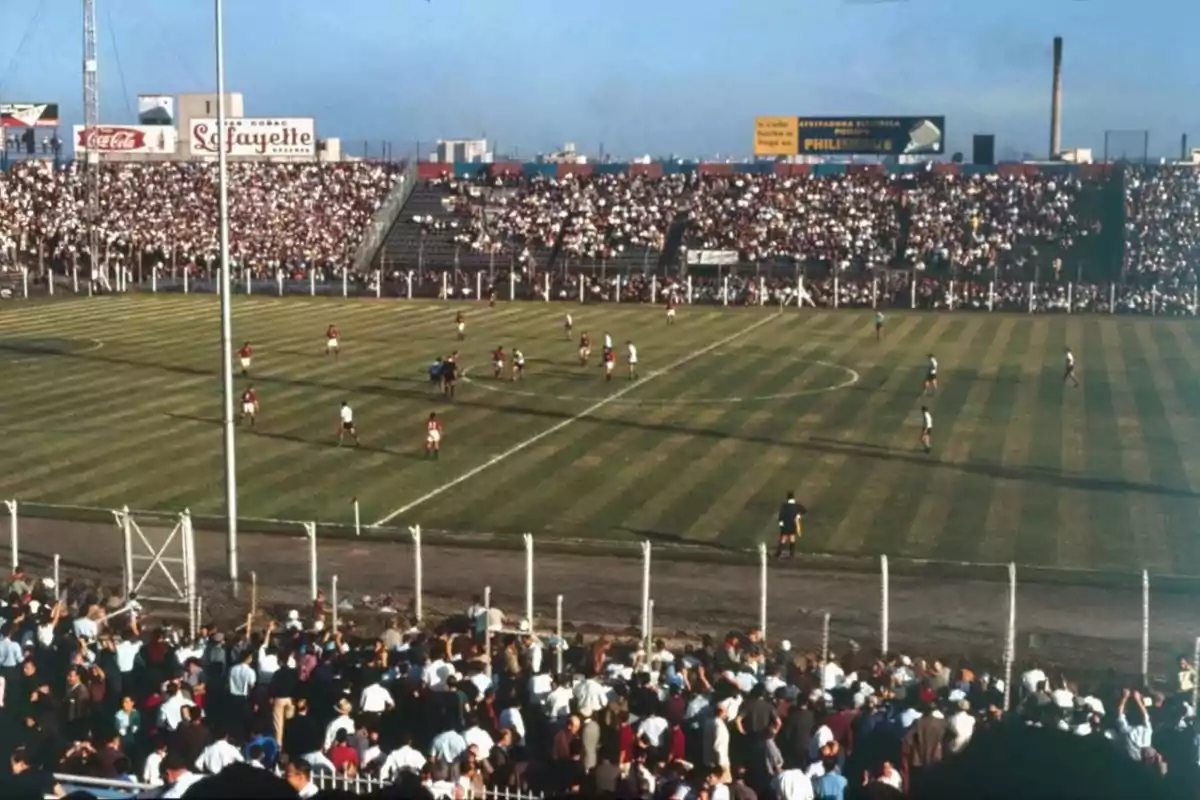 Soccer stadium full of fans with two teams playing a match on a sunny afternoon Soccer stadium full of fans with two teams playing a match on a sunny afternoon