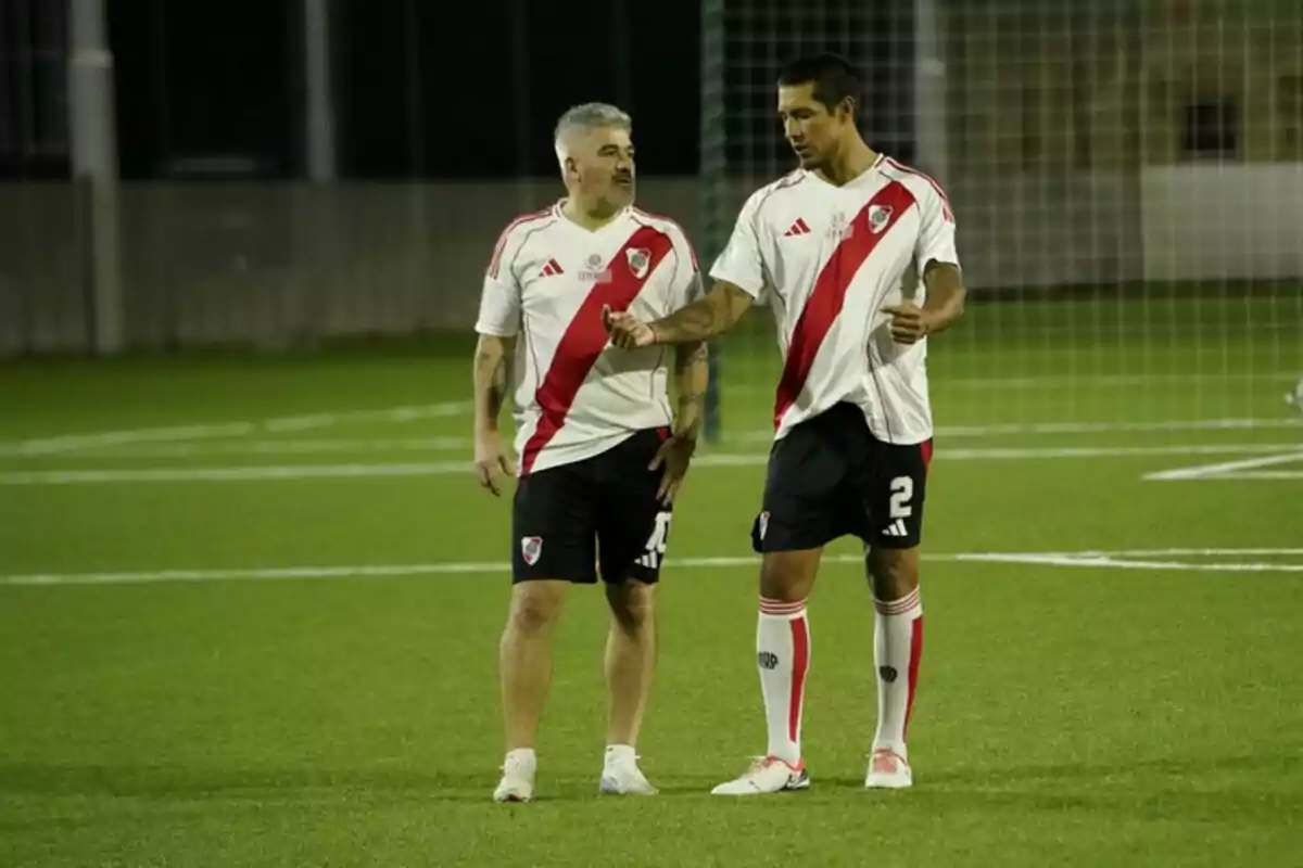 Dos hombres con uniforme de fútbol de River Plate conversan en una cancha de césped artificial Dos hombres con uniforme de fútbol de River Plate conversan en una cancha de césped artificial