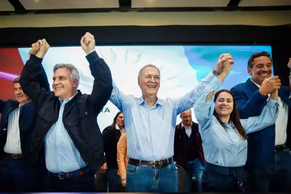 Grupo de personas sonrientes en un escenario levantando las manos en señal de celebración Grupo de personas sonrientes en un escenario levantando las manos en señal de celebración
