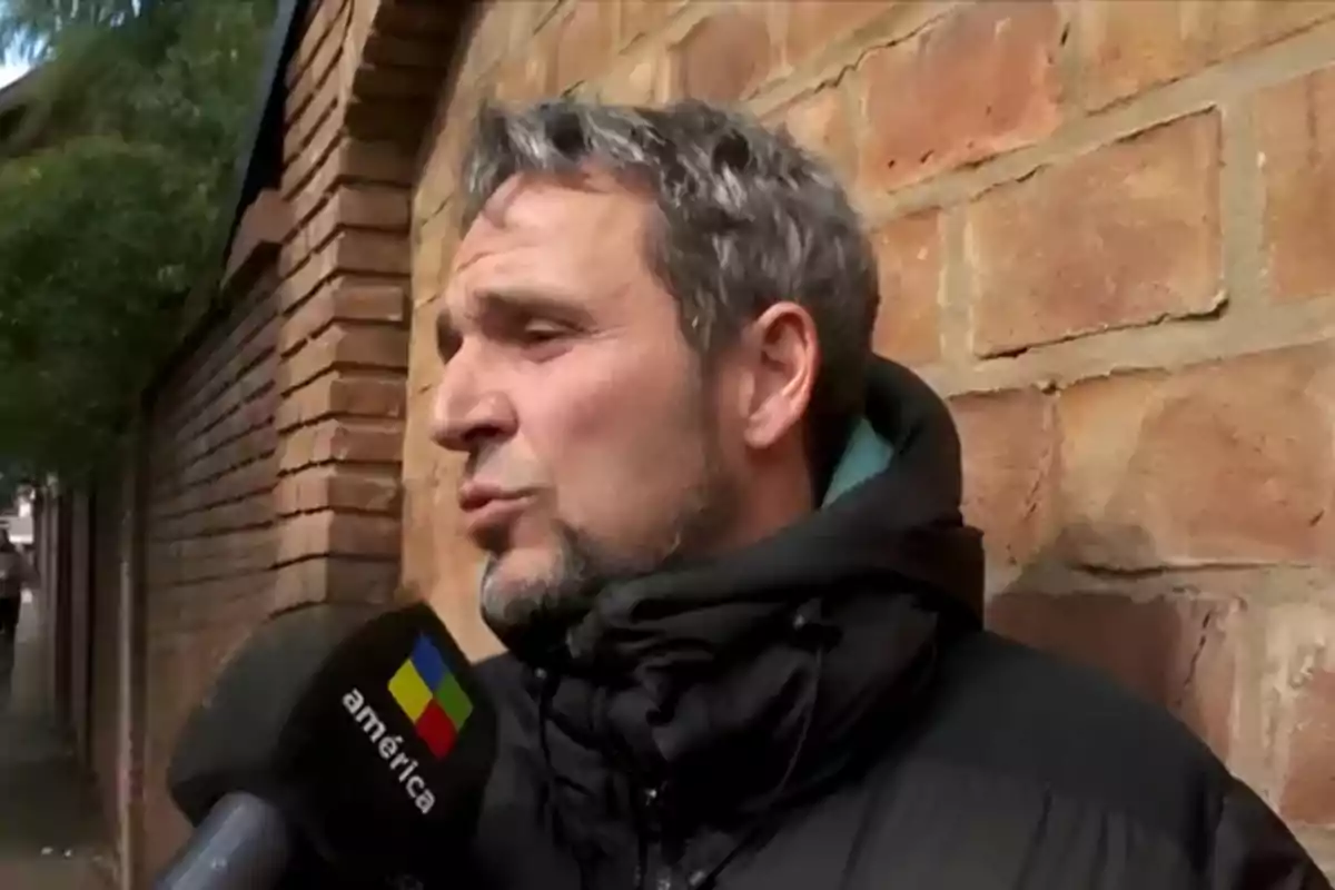 Hombre de cabello canoso y barba corta siendo entrevistado por un canal de televisión frente a una pared de ladrillos Hombre de cabello canoso y barba corta siendo entrevistado por un canal de televisión frente a una pared de ladrillos