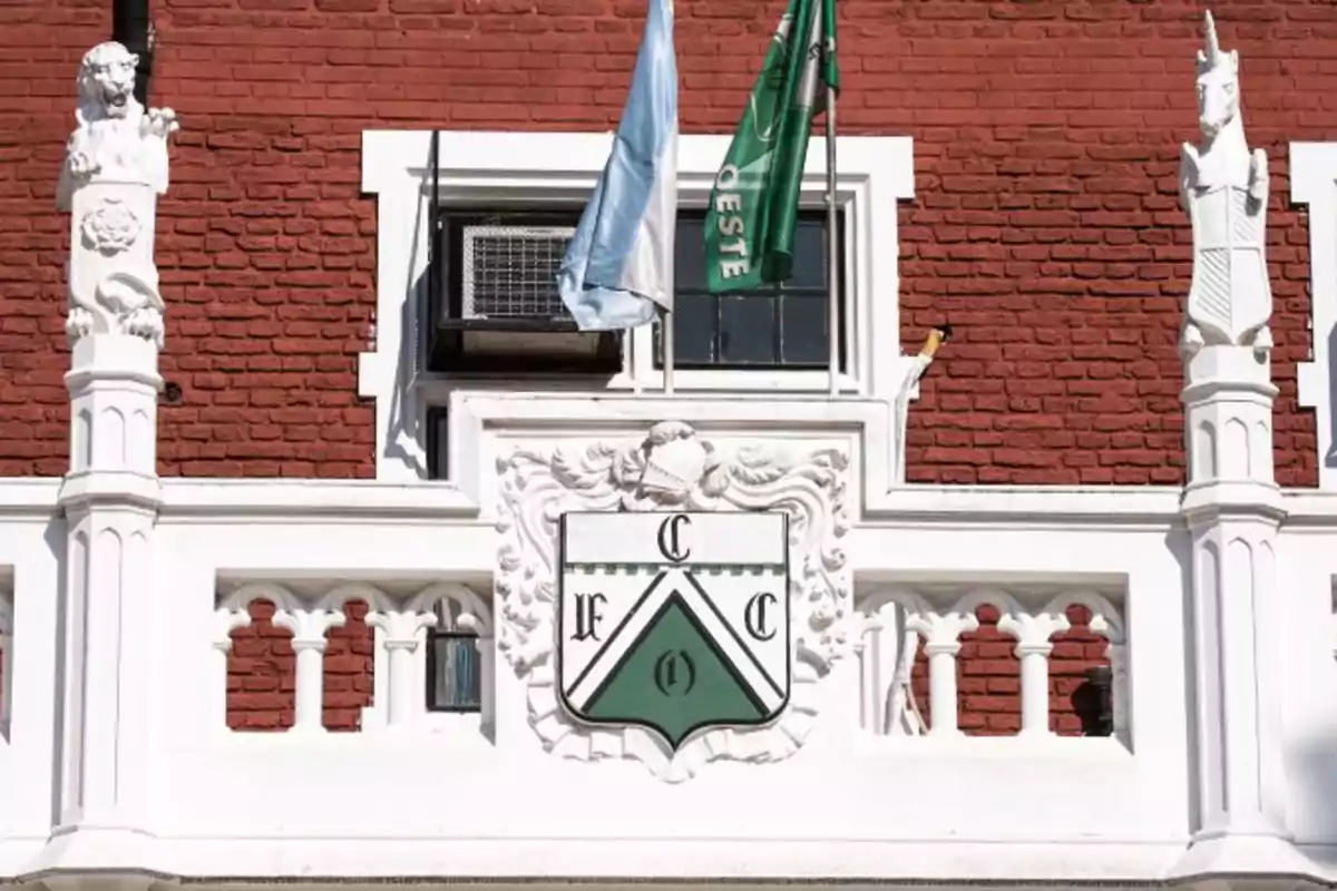 Heraldic shield on a red brick facade with white details and two flags waving above