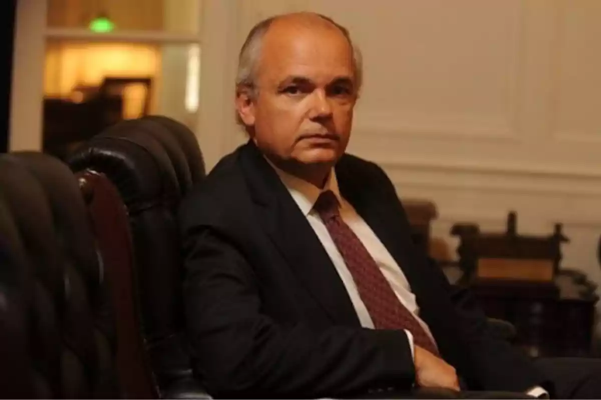 Hombre de mediana edad con traje oscuro y corbata roja sentado en una silla de oficina elegante en un ambiente formal Hombre de mediana edad con traje oscuro y corbata roja sentado en una silla de oficina elegante en un ambiente formal