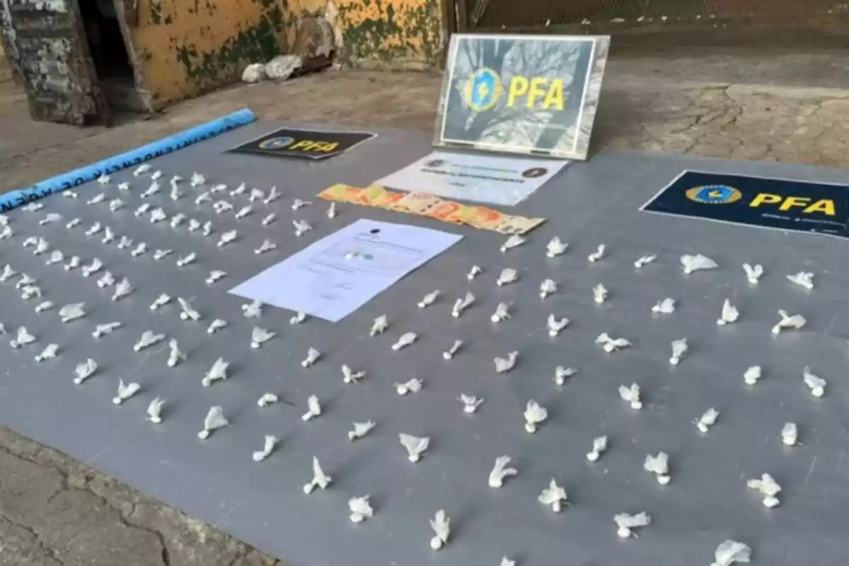 Pequeños envoltorios blancos organizados en filas sobre una mesa junto a billetes, documentos y carteles de la policía federal argentina. Pequeños envoltorios blancos organizados en filas sobre una mesa junto a billetes, documentos y carteles de la policía federal argentina.