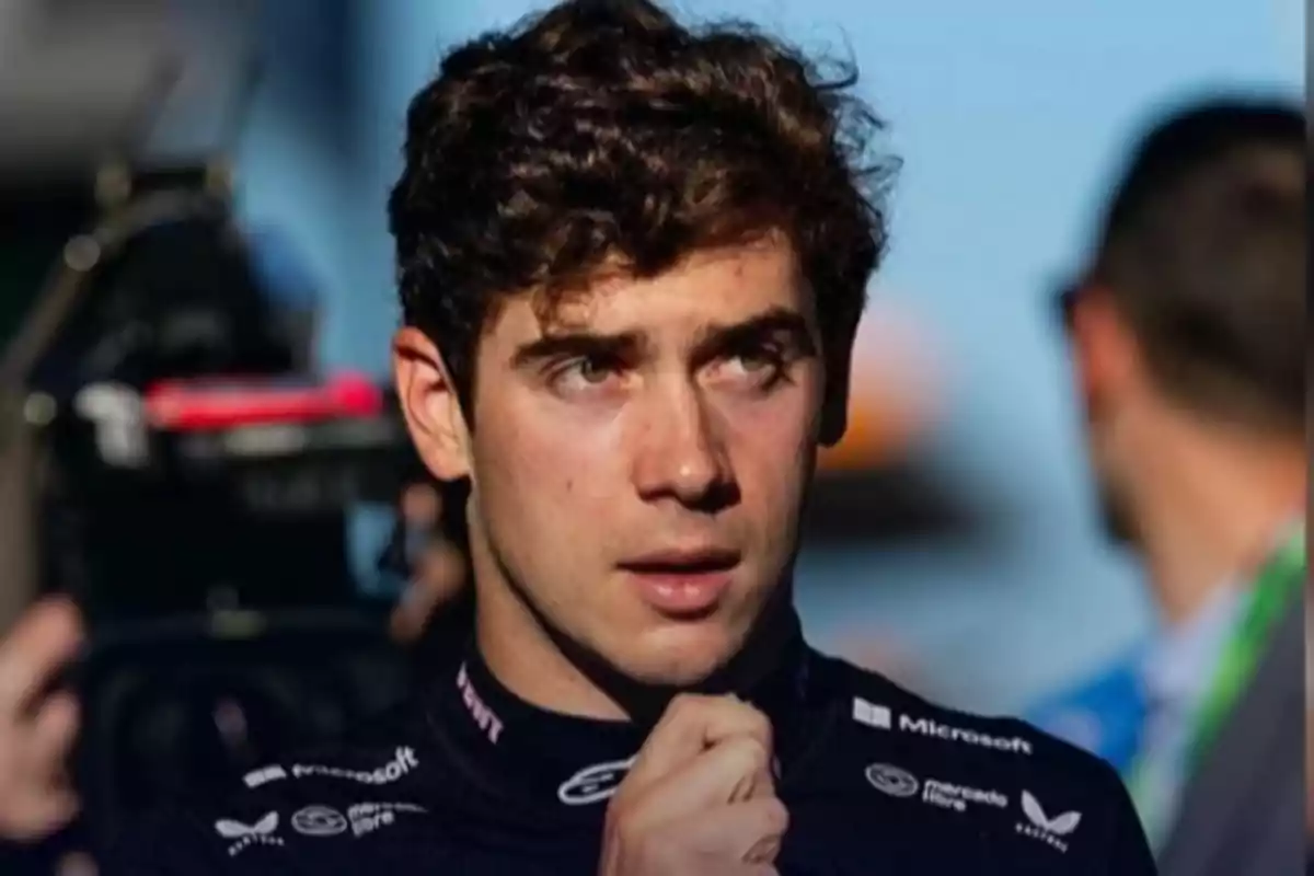 Young man with curly hair and a serious expression wearing a dark sports uniform in an outdoor setting