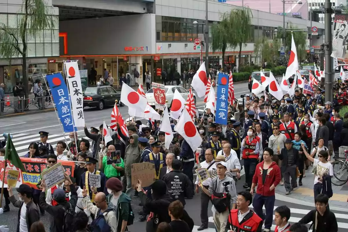 Demonstration on a street in Japan with many people carrying Japanese flags and banners while walking escorted by police officers