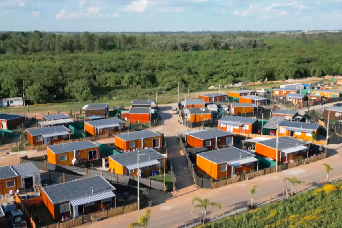 Vista aérea de un barrio con casas pequeñas de color naranja y techos grises rodeado de vegetación y árboles al fondo