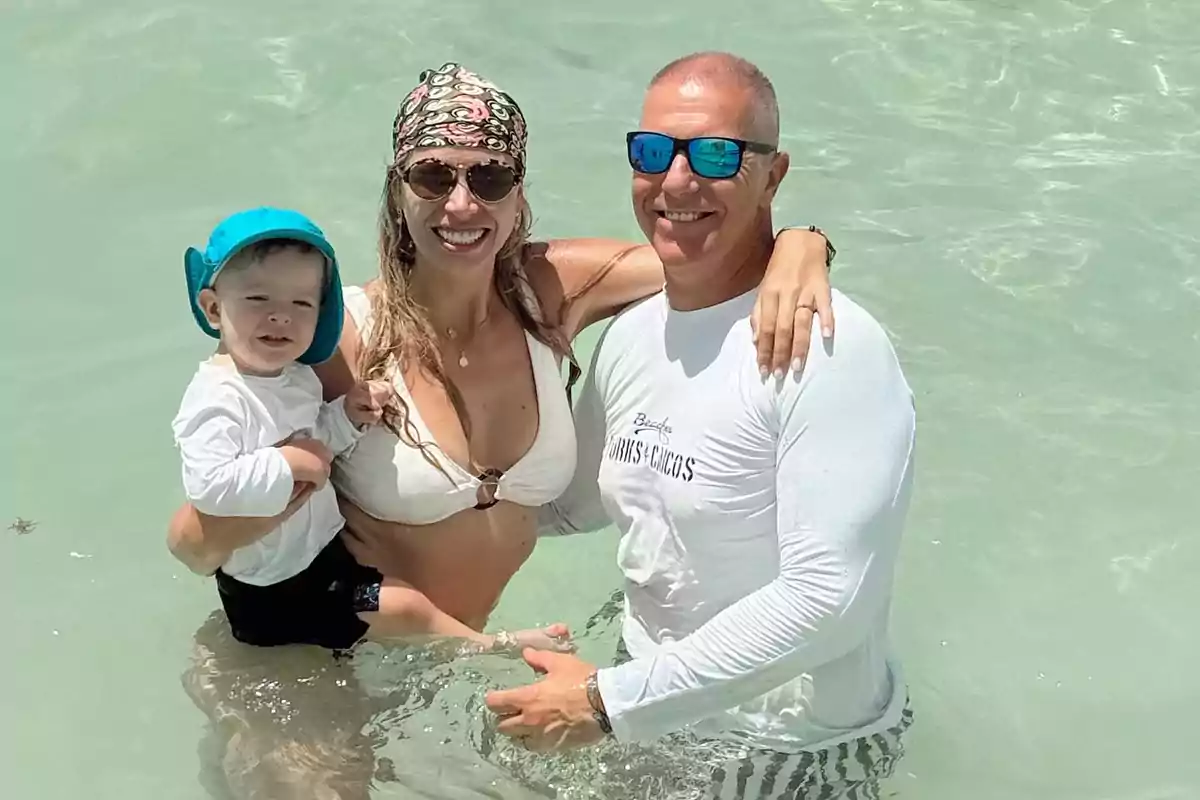Familia disfrutando de un día soleado en la playa dentro del agua con ropa de baño y sonrisas