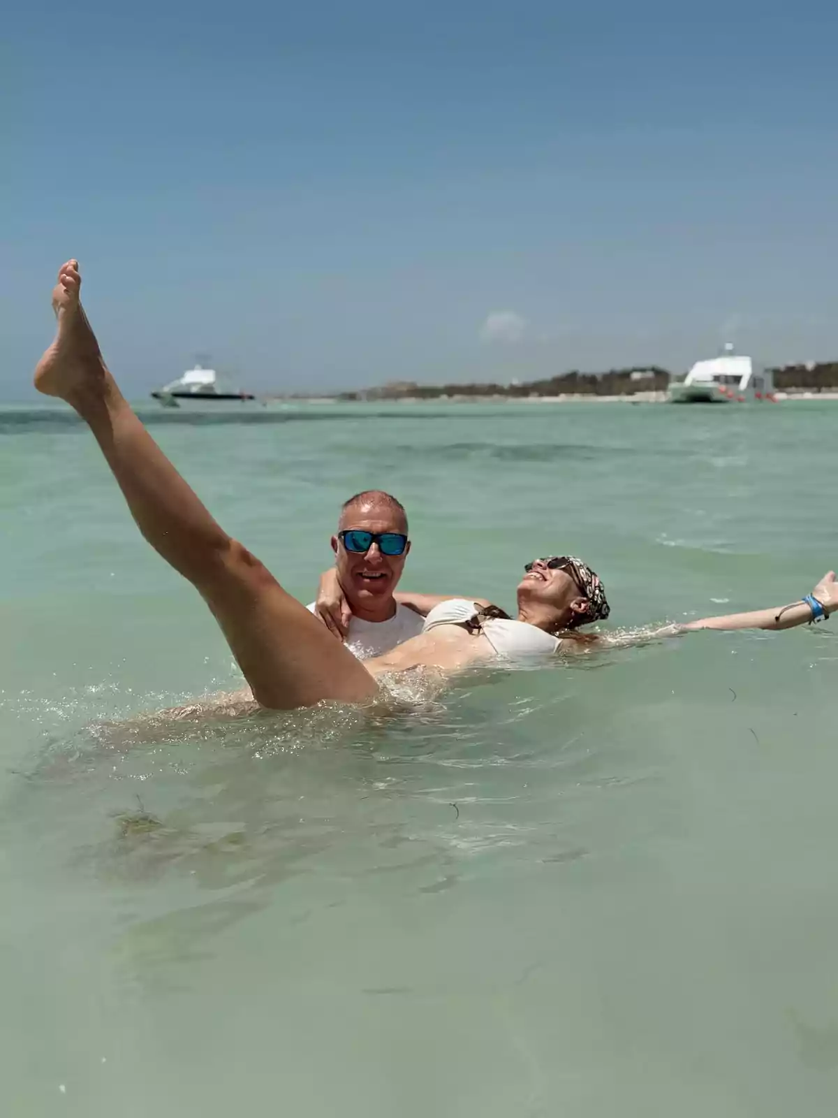 Pareja disfrutando en el mar con el hombre sosteniendo a la mujer que sonríe y levanta una pierna mientras ambos se ven felices bajo un cielo despejado Pareja disfrutando en el mar con el hombre sosteniendo a la mujer que sonríe y levanta una pierna mientras ambos se ven felices bajo un cielo despejado