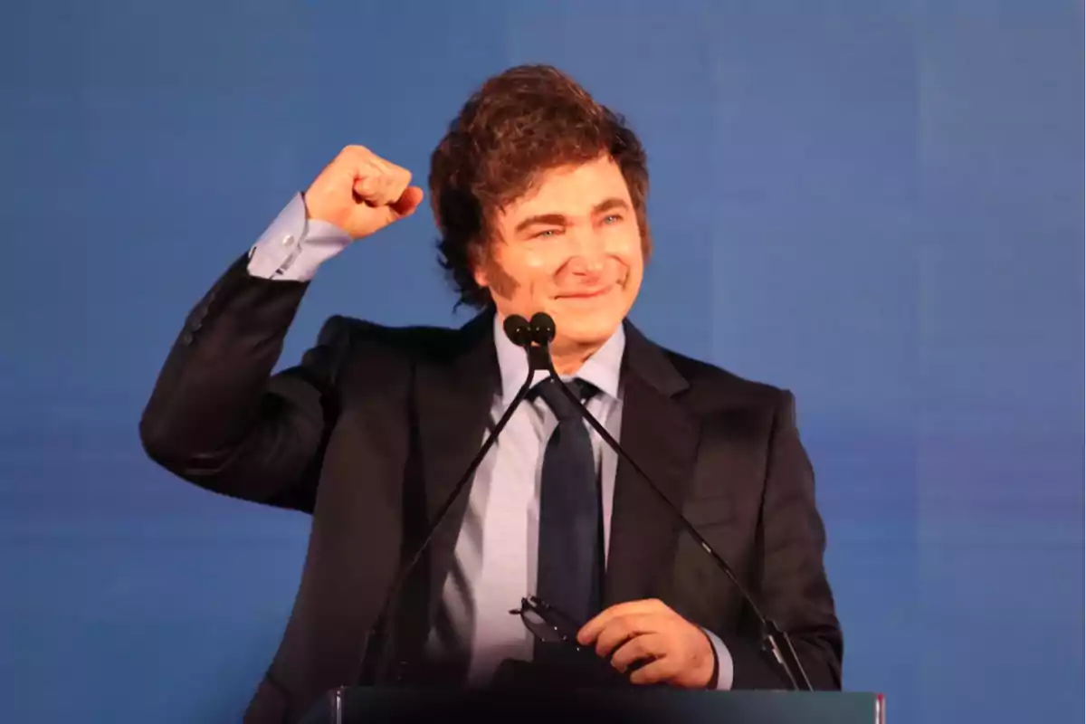 Smiling man in a suit raising his fist in celebration in front of a microphone Smiling man in a suit raising his fist in celebration in front of a microphone