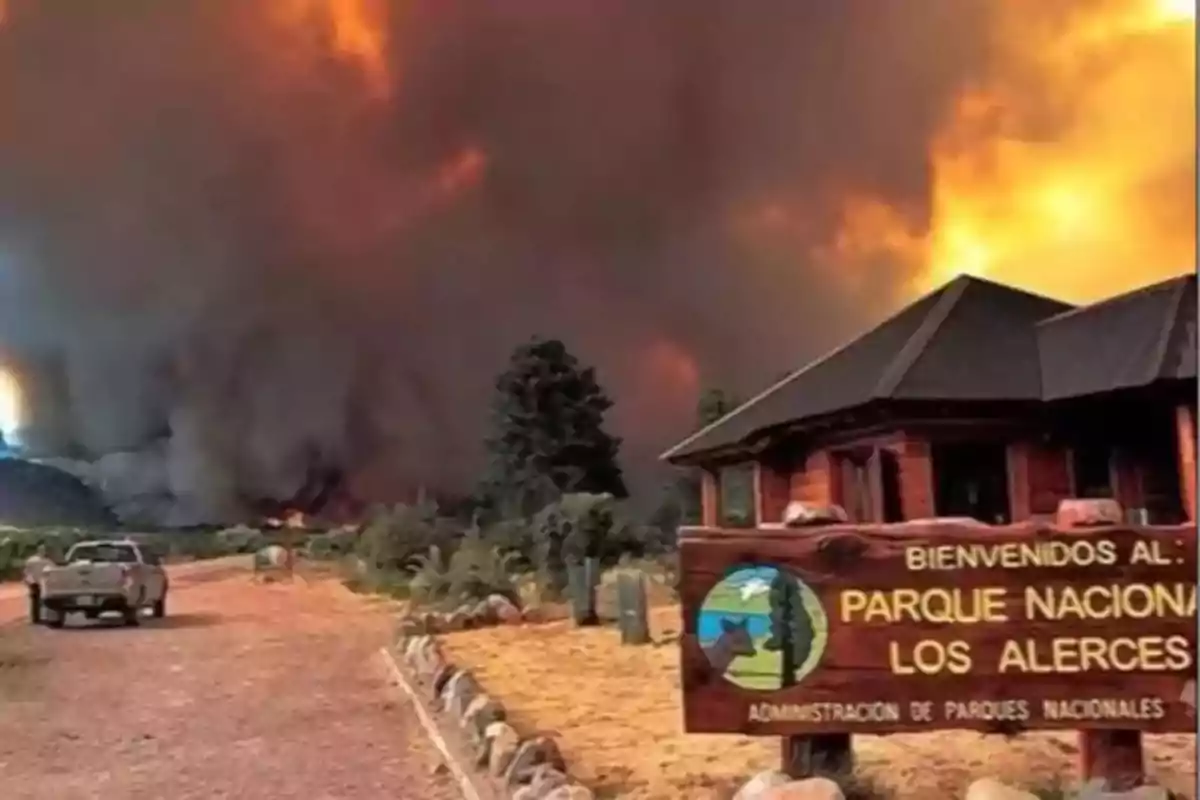 Incendio forestal de gran magnitud en el Parque Nacional Los Alerces con humo y fuego al fondo y un cartel de bienvenida en primer plano Incendio forestal de gran magnitud en el Parque Nacional Los Alerces con humo y fuego al fondo y un cartel de bienvenida en primer plano