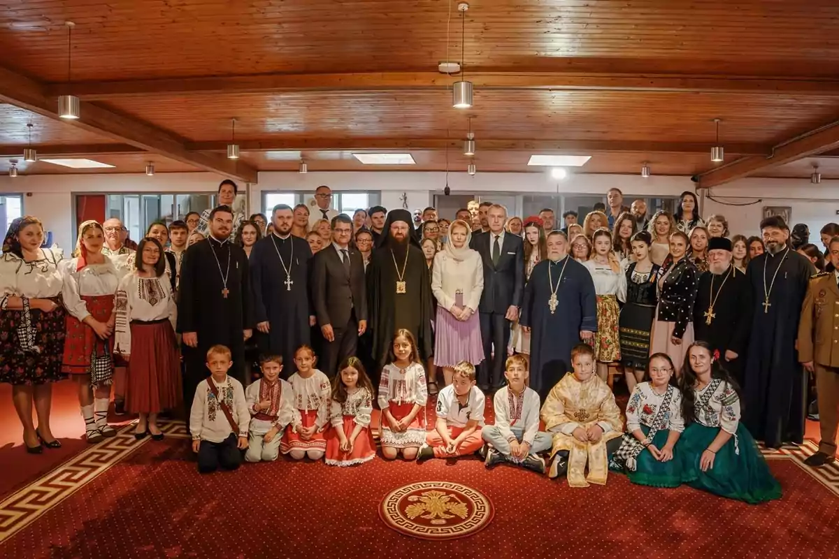 Un grupo numeroso de personas vestidas con trajes tradicionales y ropa formal posan juntas en el interior de un edificio con techo de madera Un grupo numeroso de personas vestidas con trajes tradicionales y ropa formal posan juntas en el interior de un edificio con techo de madera