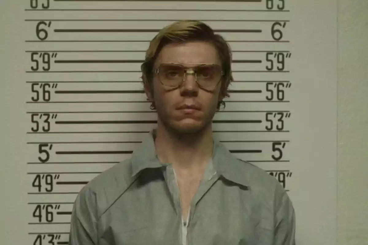 Man with glasses and blond hair posing in front of a height measurement wall in what appears to be a mugshot. Man with glasses and blond hair posing in front of a height measurement wall in what appears to be a mugshot.