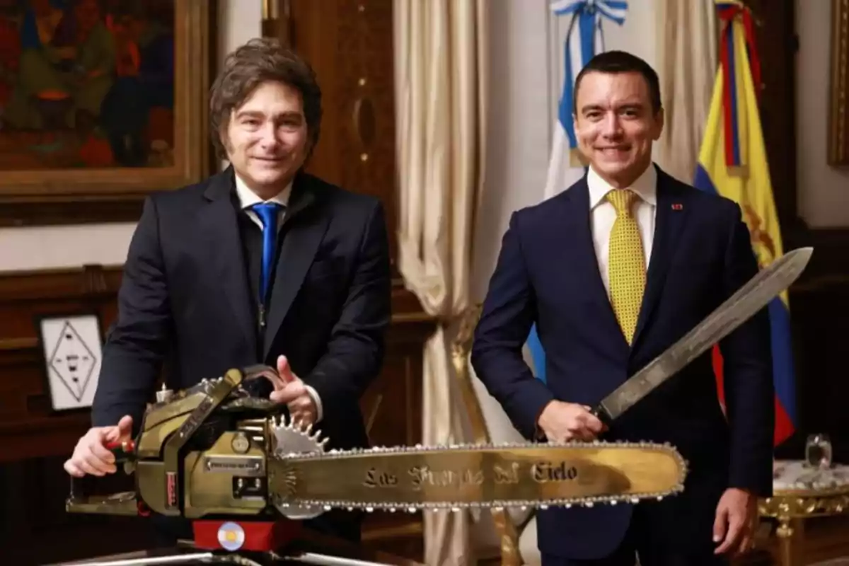 Dos hombres de traje posan sonrientes en una oficina elegante uno sostiene una motosierra dorada y el otro una espada larga con banderas de Argentina y Ecuador al fondo