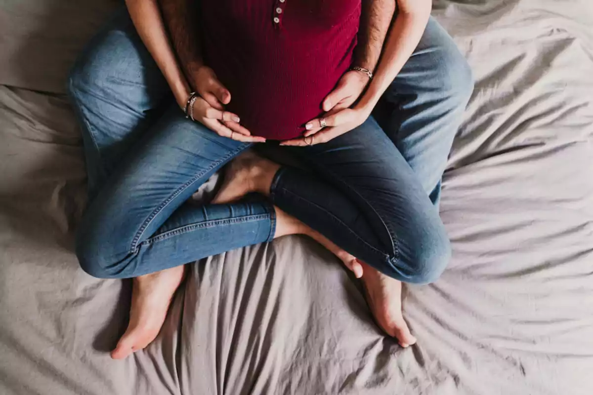 Couple sitting on the bed hugging a pregnant woman's belly Couple sitting on the bed hugging a pregnant woman's belly