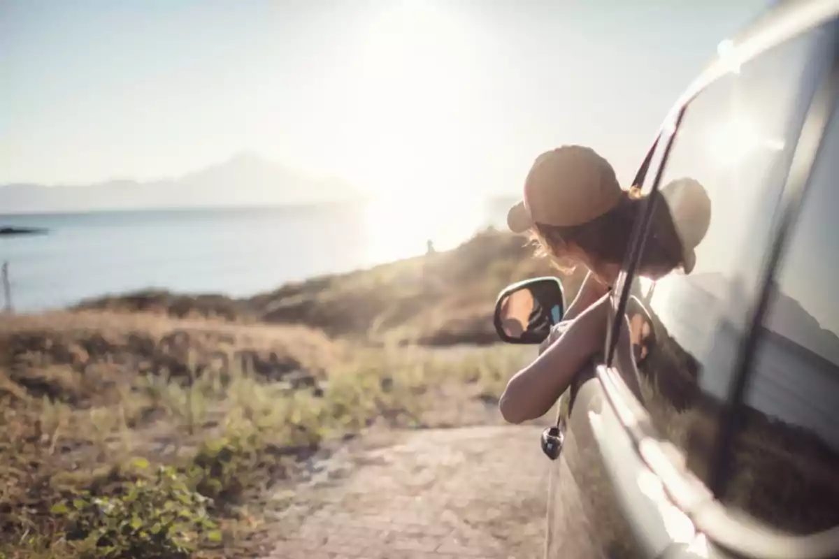 Person leaning out the window of a car enjoying the view of the sea at sunset Person leaning out the window of a car enjoying the view of the sea at sunset