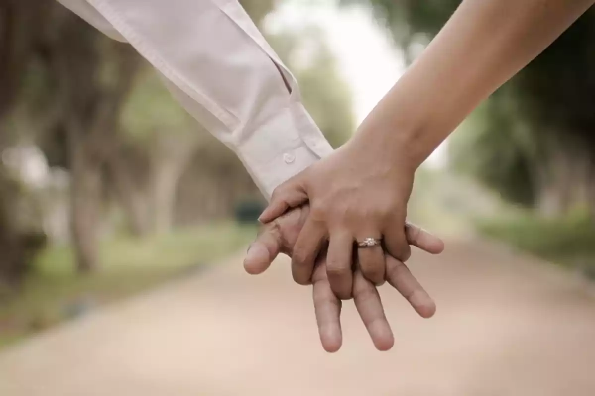 Hands of a couple intertwined, showing an engagement ring on an outdoor path Hands of a couple intertwined, showing an engagement ring on an outdoor path