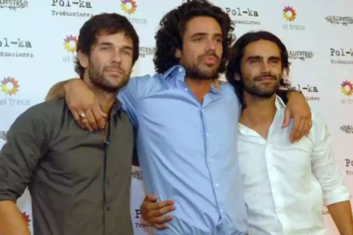 Three men pose together with their arms around each other in front of a backdrop with Pol-ka and El Trece logos. Three men pose together with their arms around each other in front of a backdrop with Pol-ka and El Trece logos.