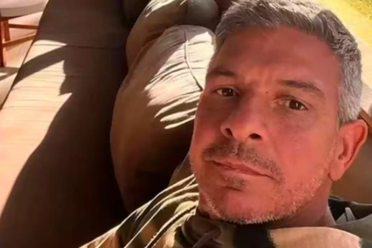 Gray-haired man lying on a brown sofa looking at the camera Gray-haired man lying on a brown sofa looking at the camera
