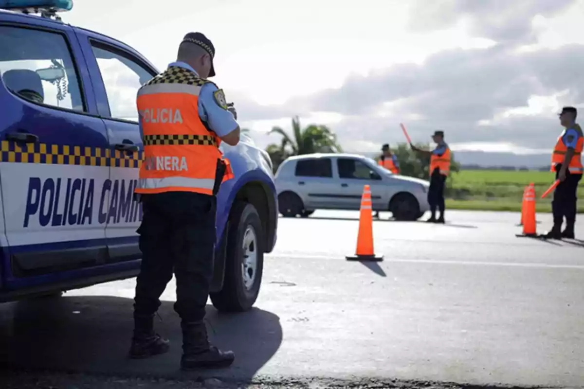 Policías camineros realizan un control vehicular en una carretera utilizando conos naranjas y chalecos reflectantes junto a una patrulla y un auto detenido